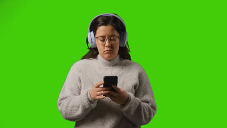 Junge-Frau-Mit-Kabellosen-Kopfhörern,-Die-Musik-Vom-Mobiltelefon-Vor-Dem-Grünen-Studiobildschirm-Streamen-2